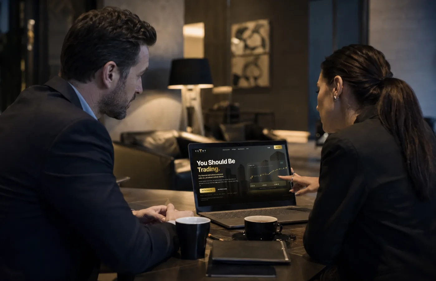 Two people reviewing the You Should Be Trading site together on a laptop
